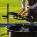 Man placerar grillspett på höjdjusterbart galler över eldfat från Cook King Bandito.