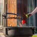 Man lägger paprika på grillgaller ovanför eldfat från Cook King Bandito i kvällssol.