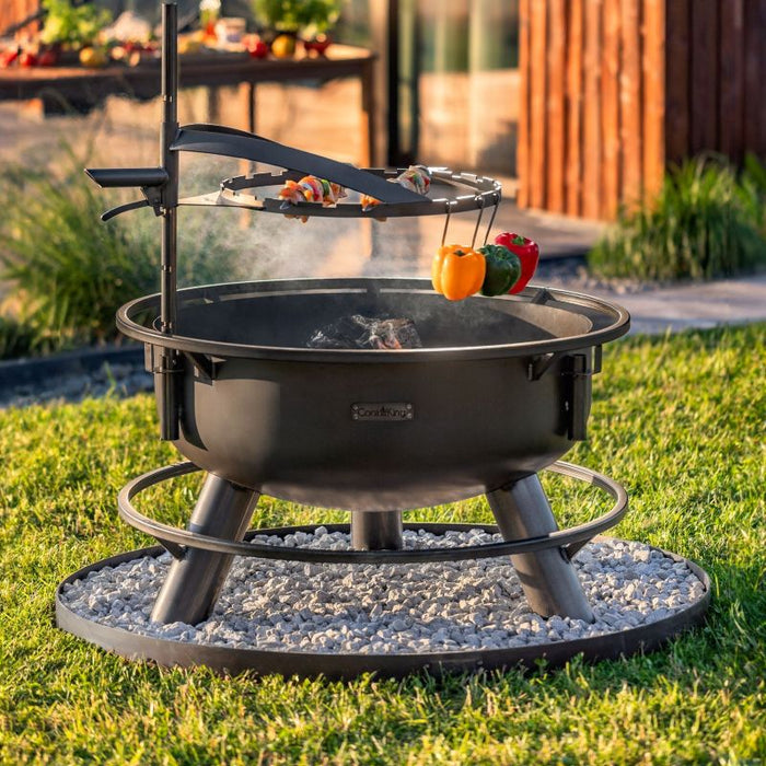 Grillspett och grönsaker på höjdjusterbart galler ovanför Bandito eldfat i trädgård.