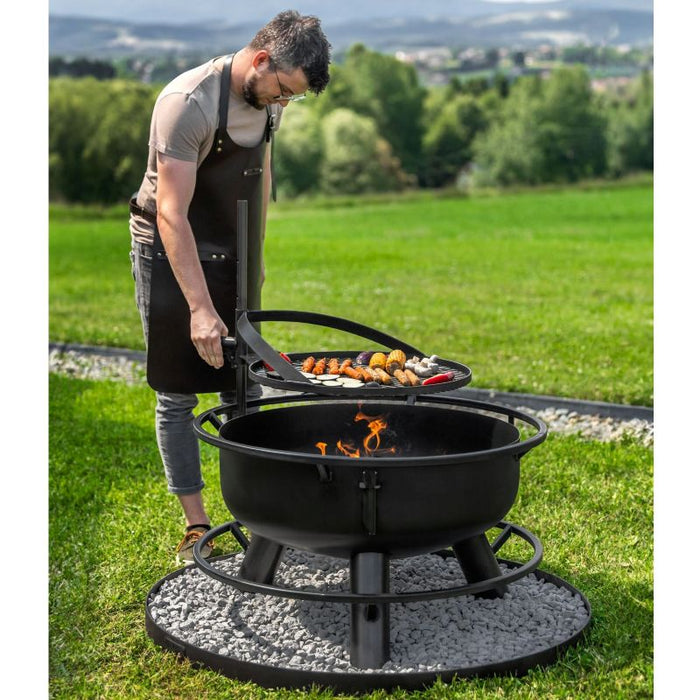 Man justerar grillhöjden på Cook King Bandito eldfat under grillning.