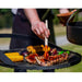 Grillgaller fyllt med kött och grönsaker över eld, där någon penslar sås på revbensspjäll