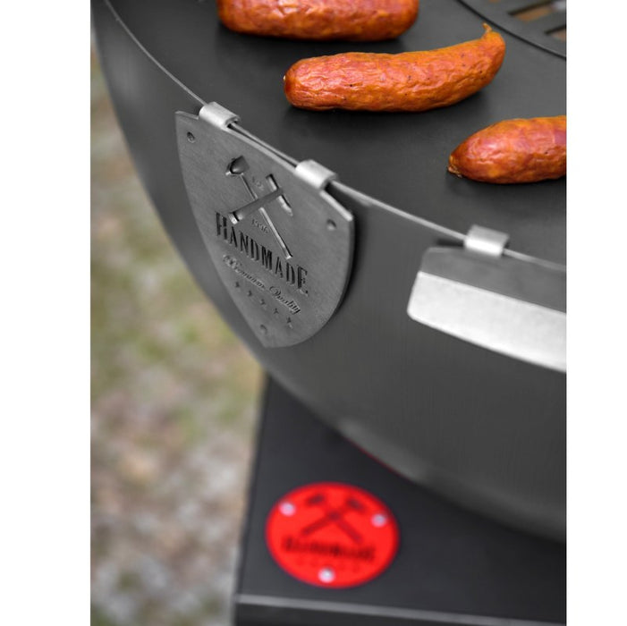 Detaljbild på Cook King Santos grill, med handgjord kvalitetsmärkning och grillad korv på plattan.