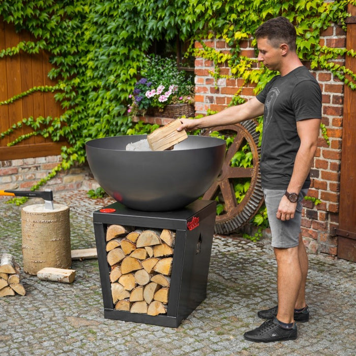 Person som lägger ved i Santos eldfat och grill från Cook King